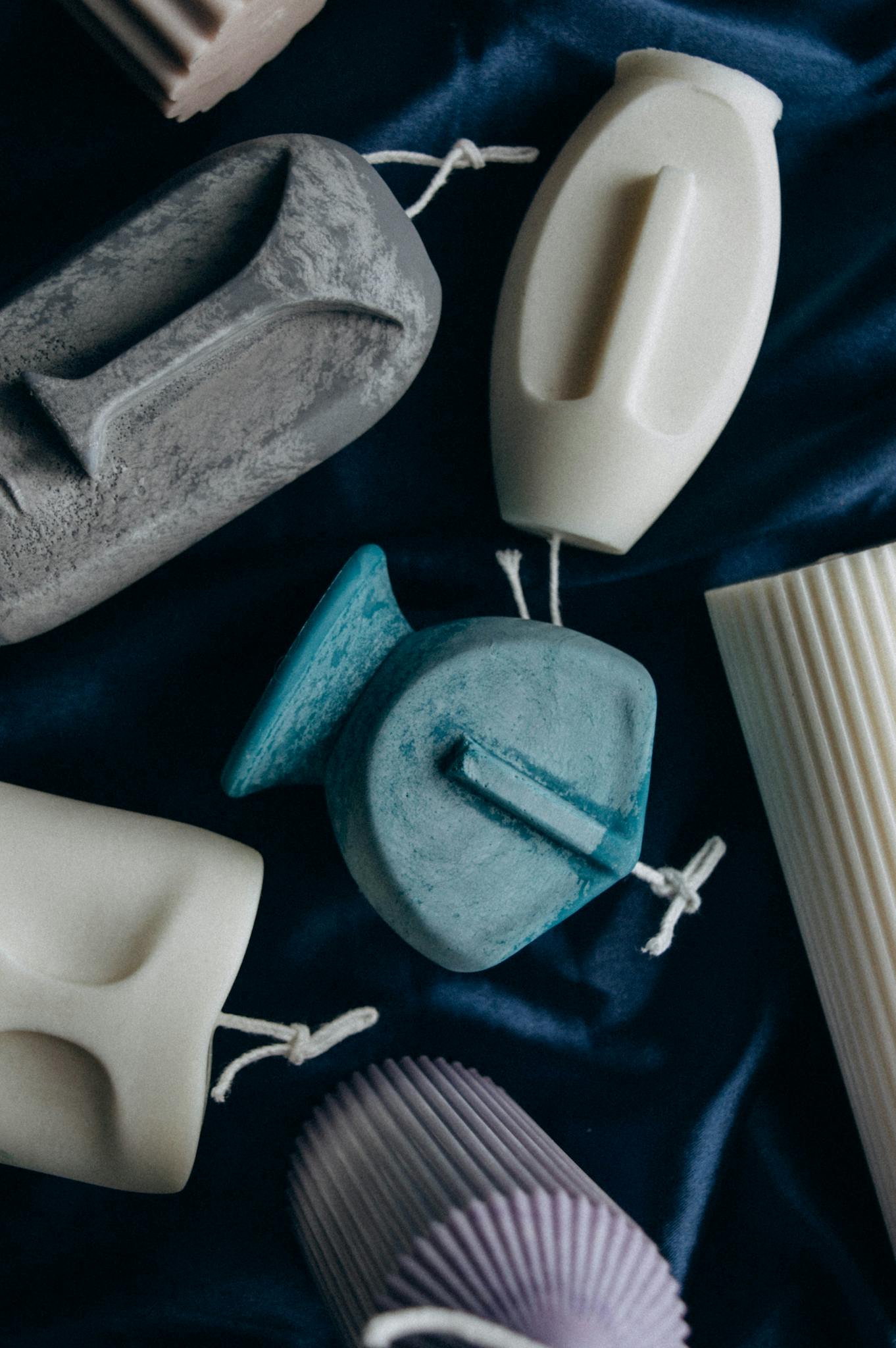 A collection of uniquely shaped homemade candles on a dark textured fabric background.